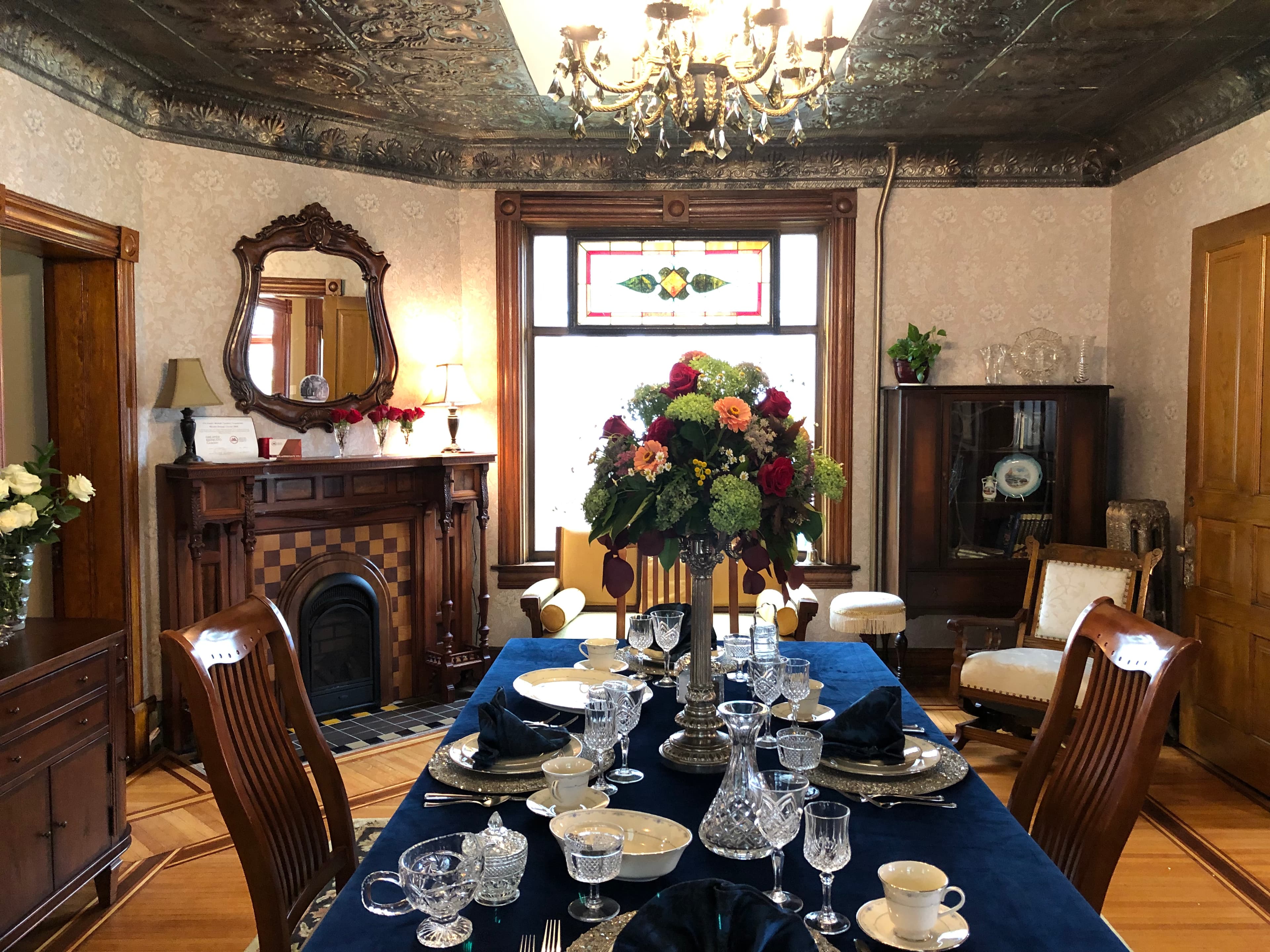 A beautifully set dining room featuring a floral centerpiece, elegant tableware, and vintage furnishings.