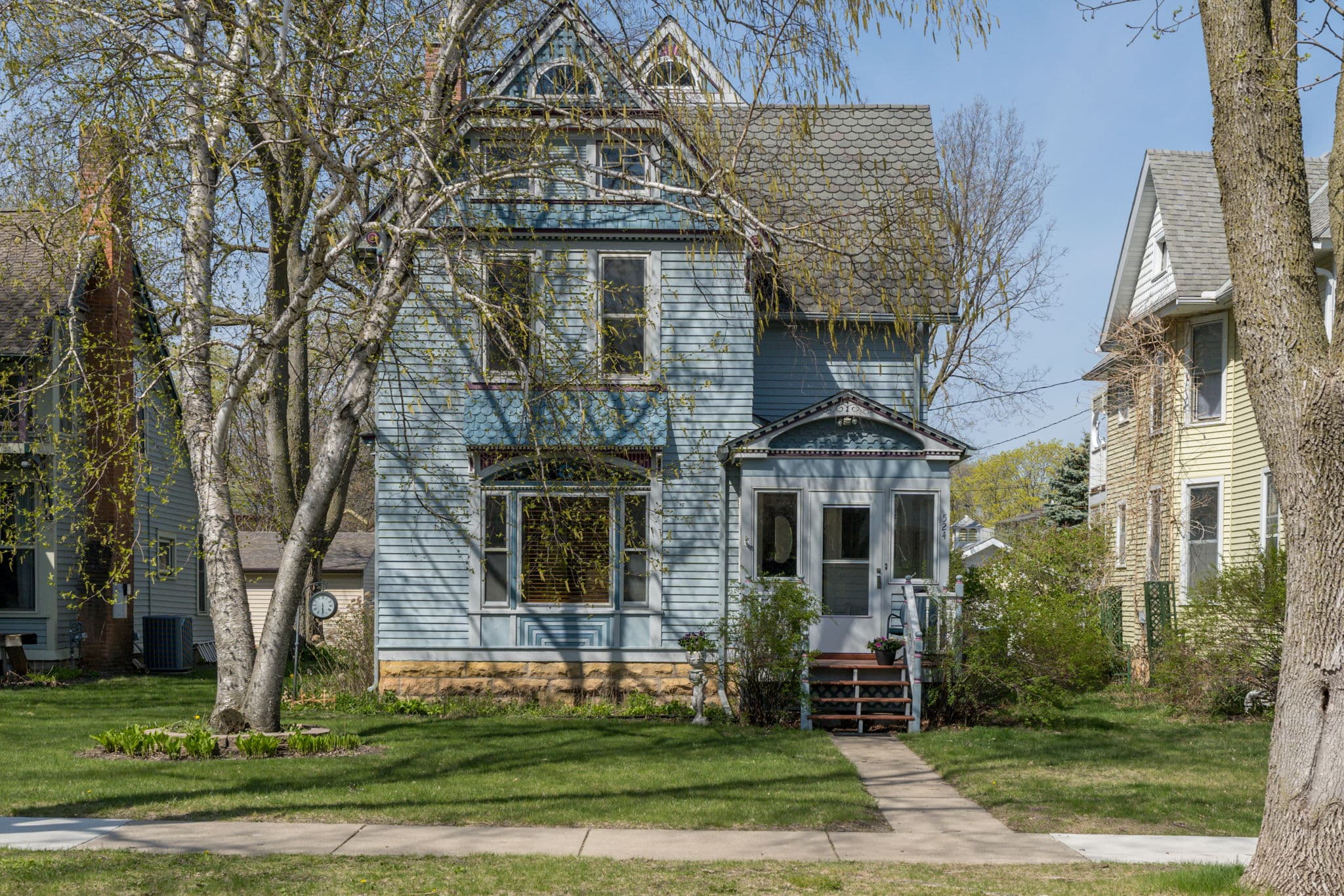 A blue Victorian-style house with a front porch and surrounding greenery.