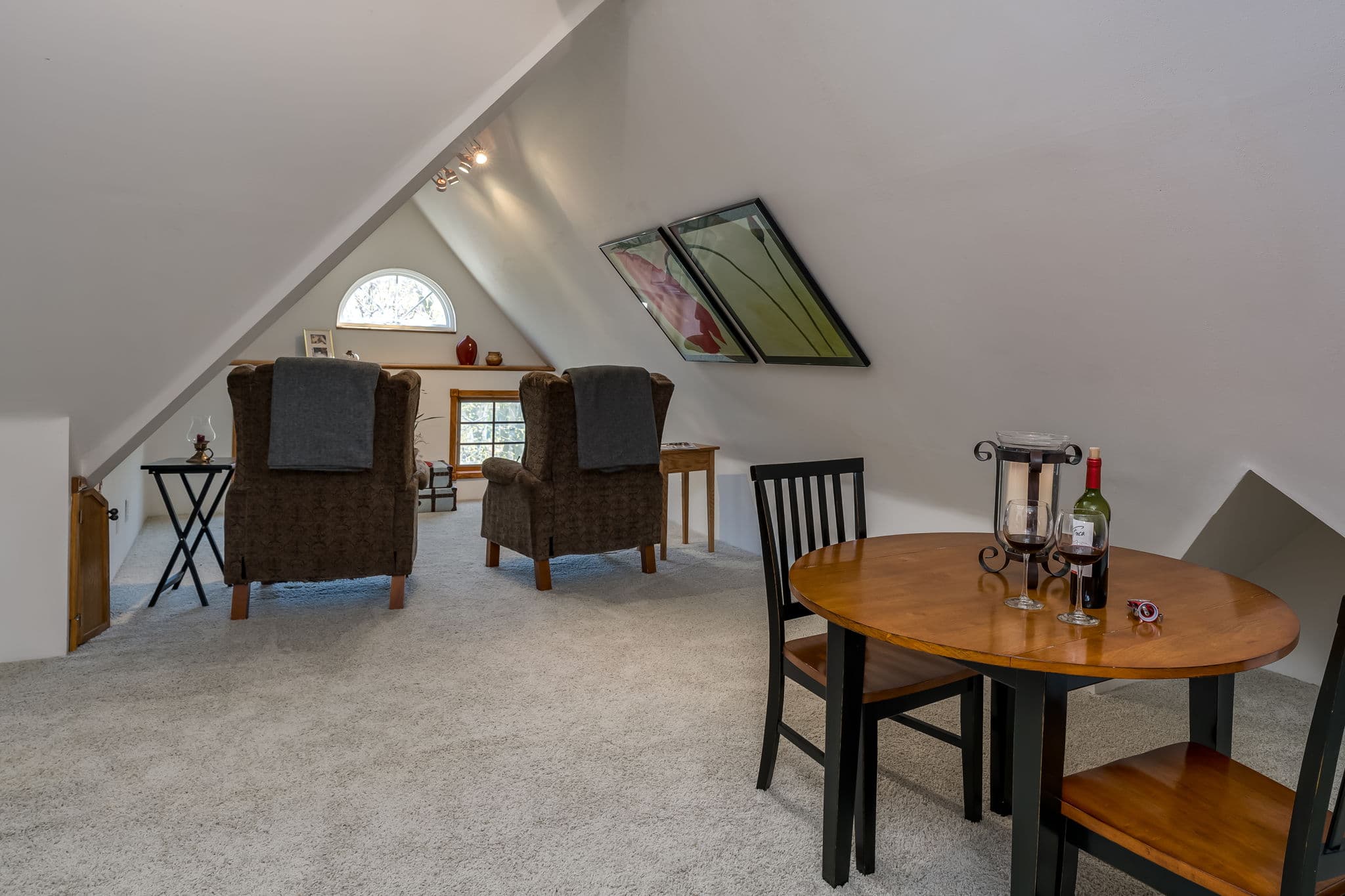 A cozy loft area featuring two armchairs, a dining table, and a large window.