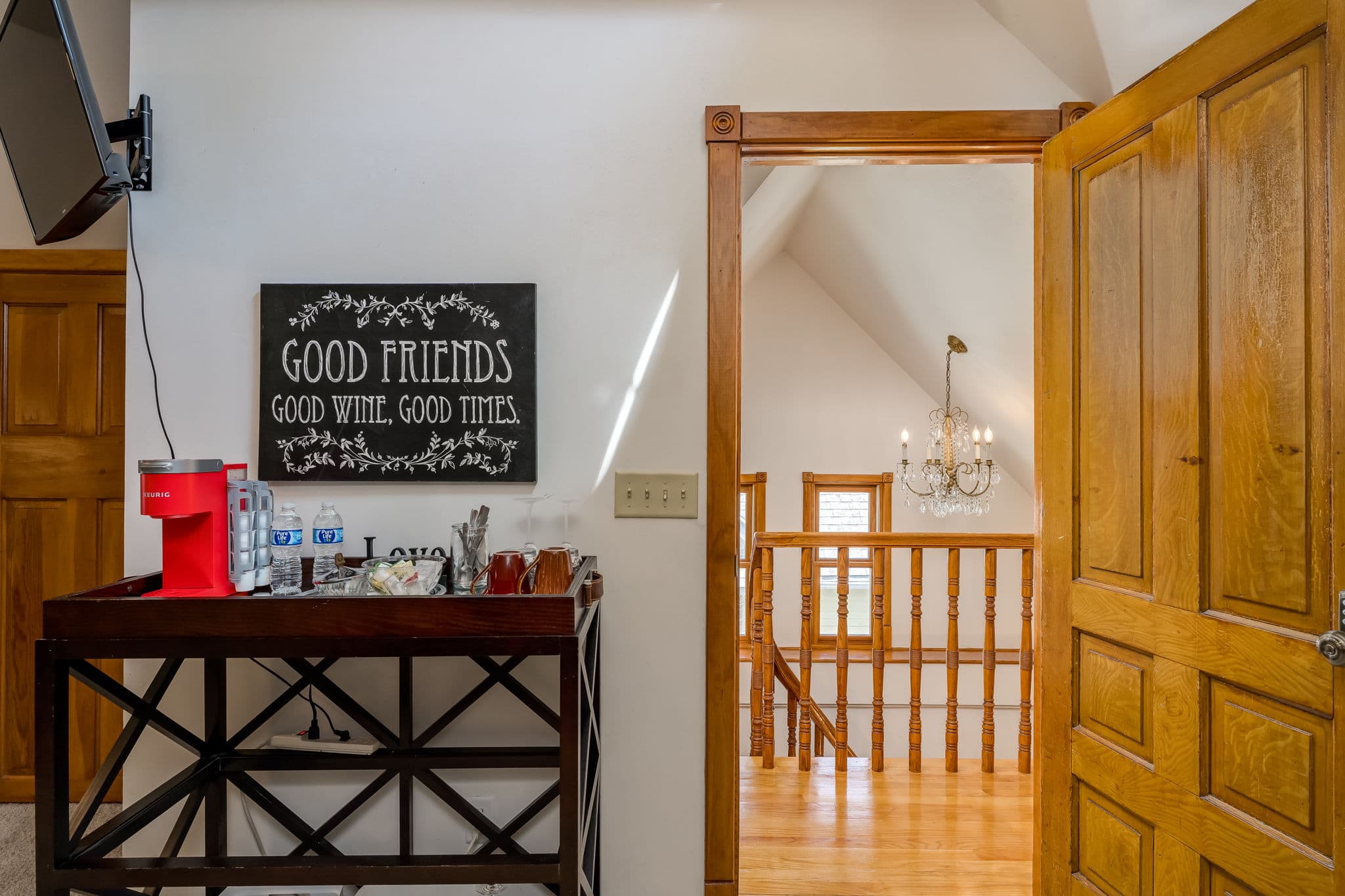 A welcoming entryway features a sign reading "Good Friends, Good Wine, Good Times" beside a bar cart and a staircase leading to a well-lit loft.
