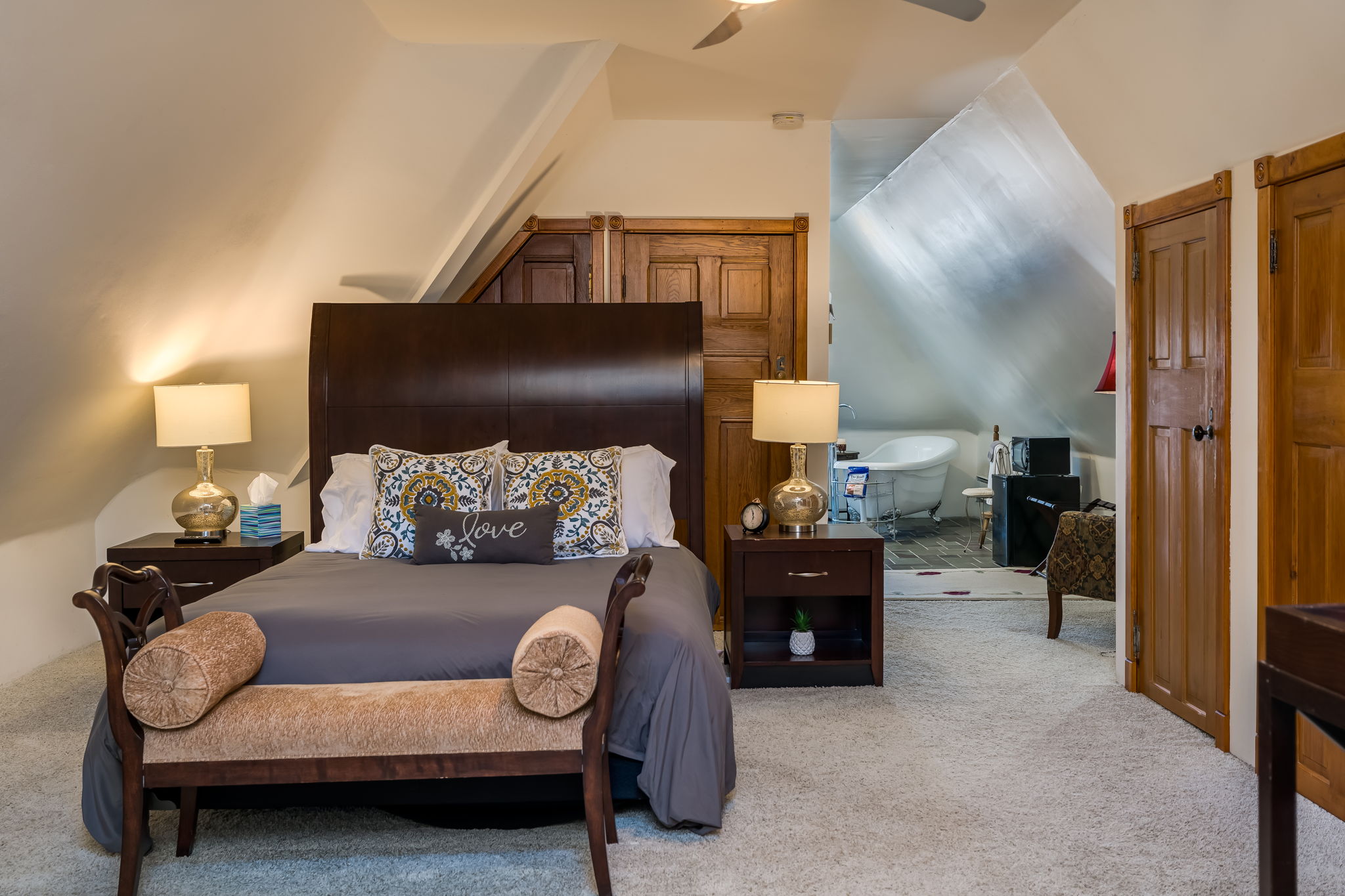 Cozy attic bedroom with a wooden bed, decorative pillows, and warm lighting.