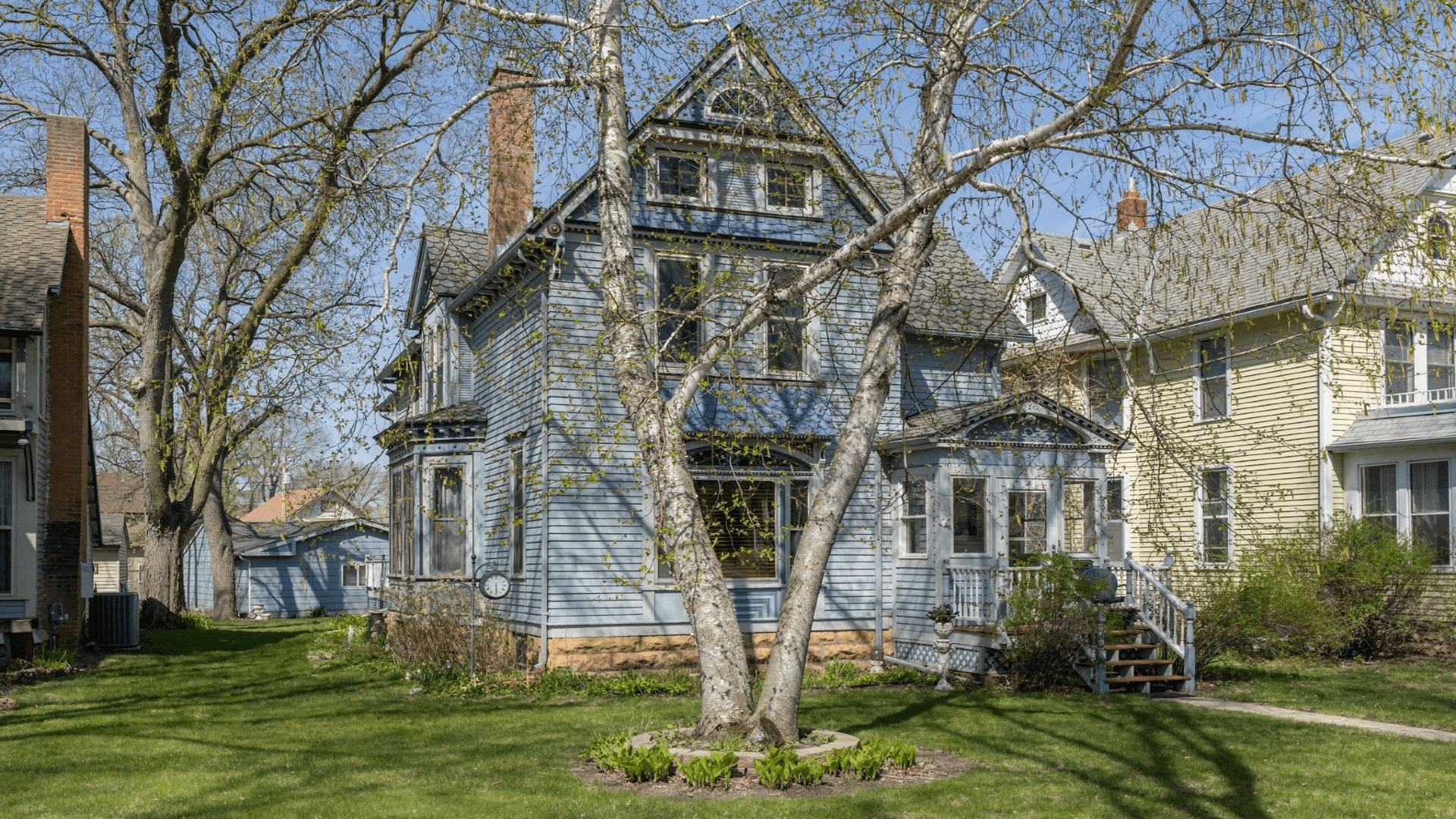 A historic blue Victorian house surrounded by lush green grass and trees.