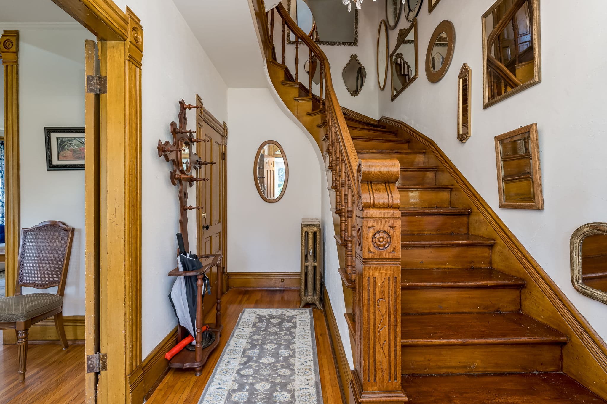 A wooden staircase leads to a second floor, surrounded by mirrors and framed artwork in a warmly lit hallway.