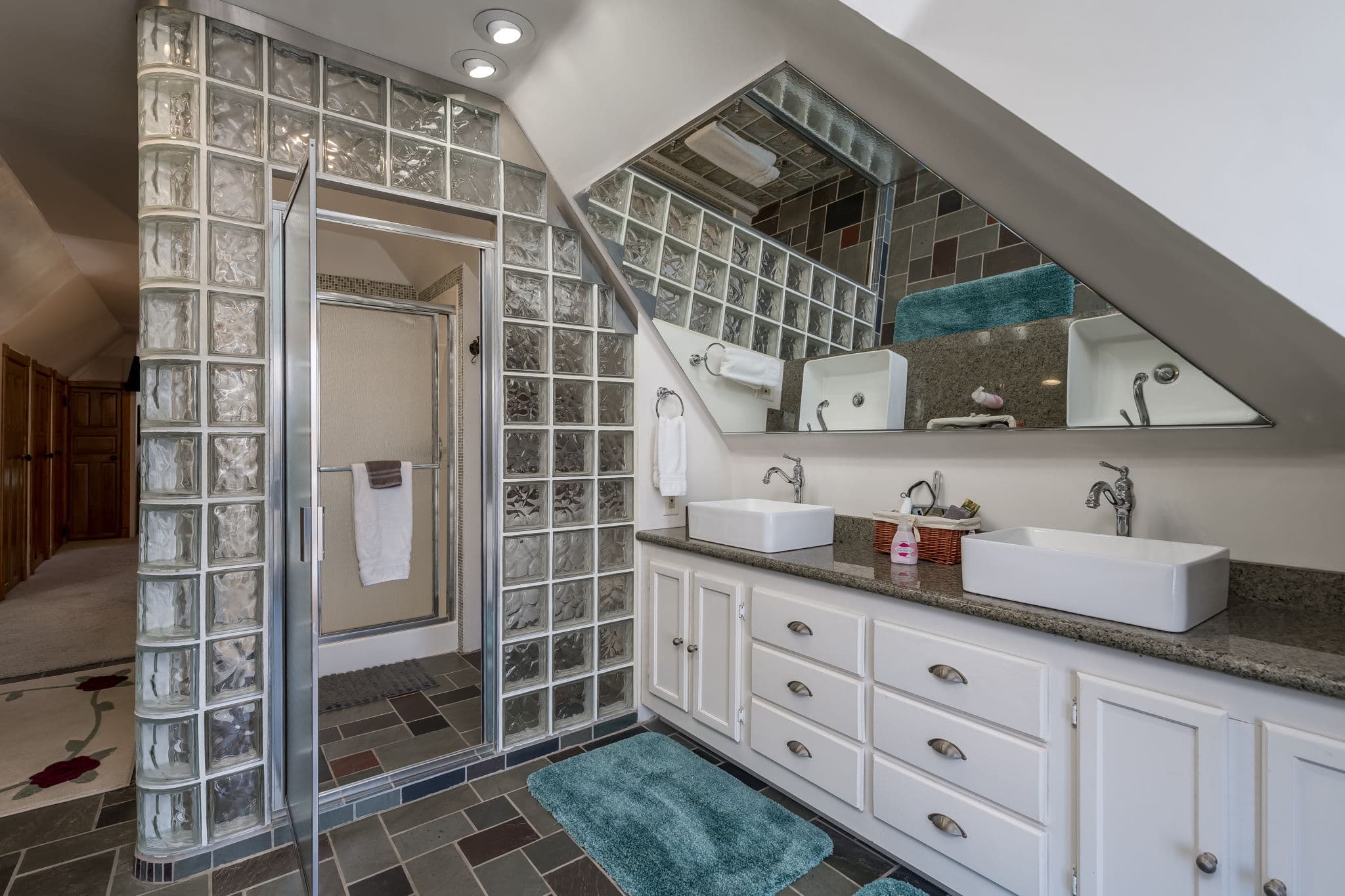 A modern bathroom featuring a glass block shower, dual sinks, and stylish gray and white decor.