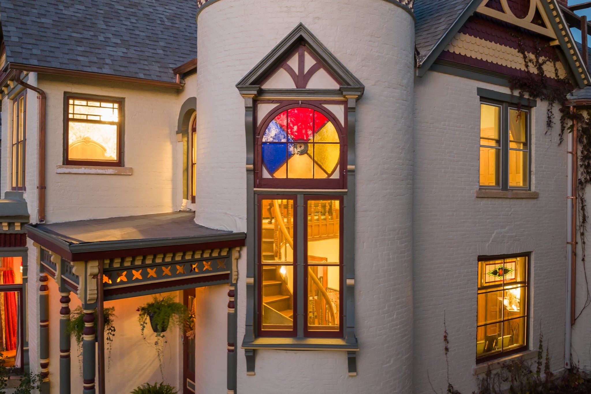 A Victorian-style house with colorful stained glass windows illuminated at dusk.