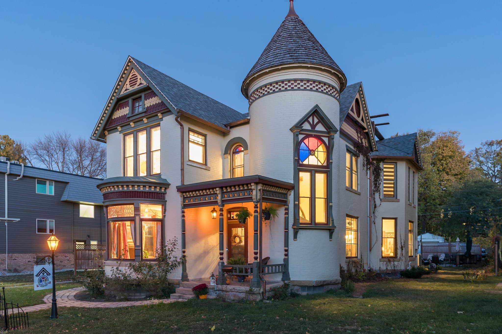 A beautifully detailed Victorian house with a turret and colorful stained glass windows, illuminated at dusk.