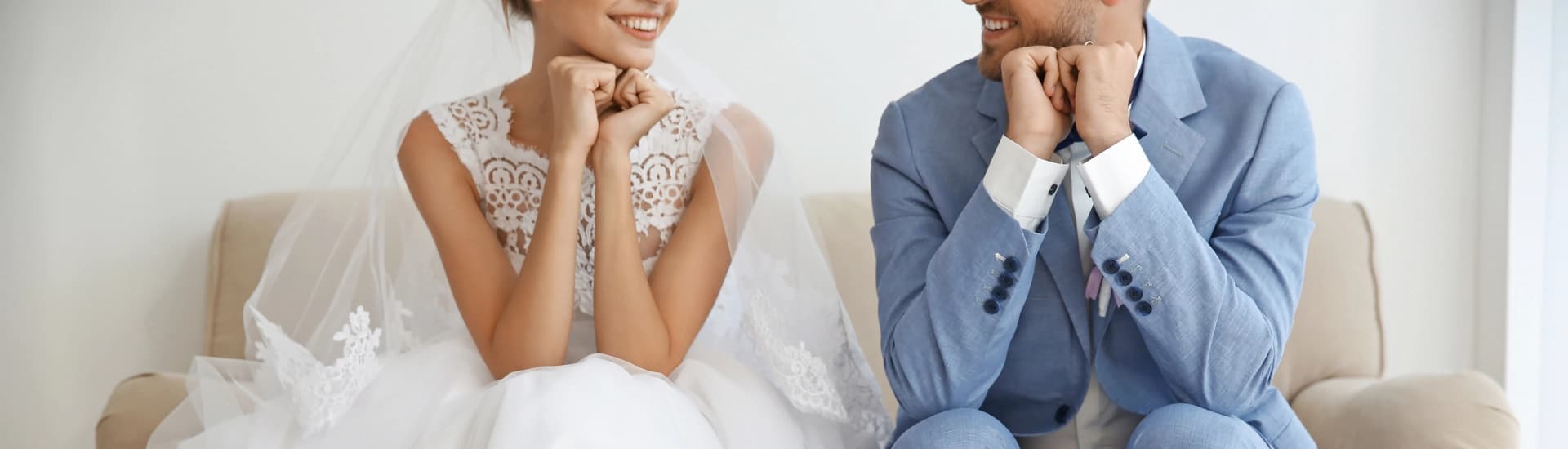 A happy newlywed couple sits together, smiling and holding their hands under their chins.