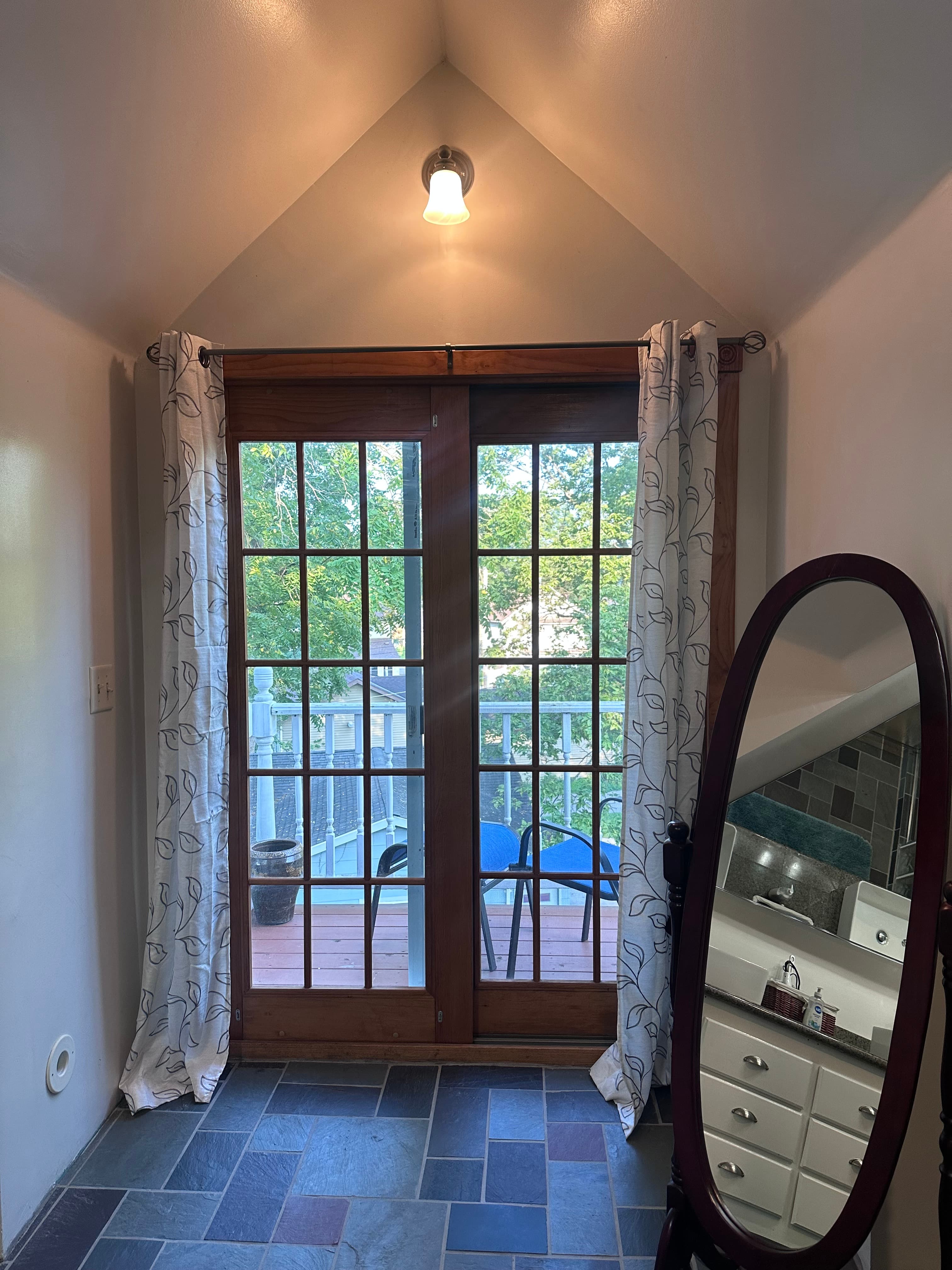 A well-lit hallway features double glass doors leading to a deck and a decorative mirror positioned nearby.