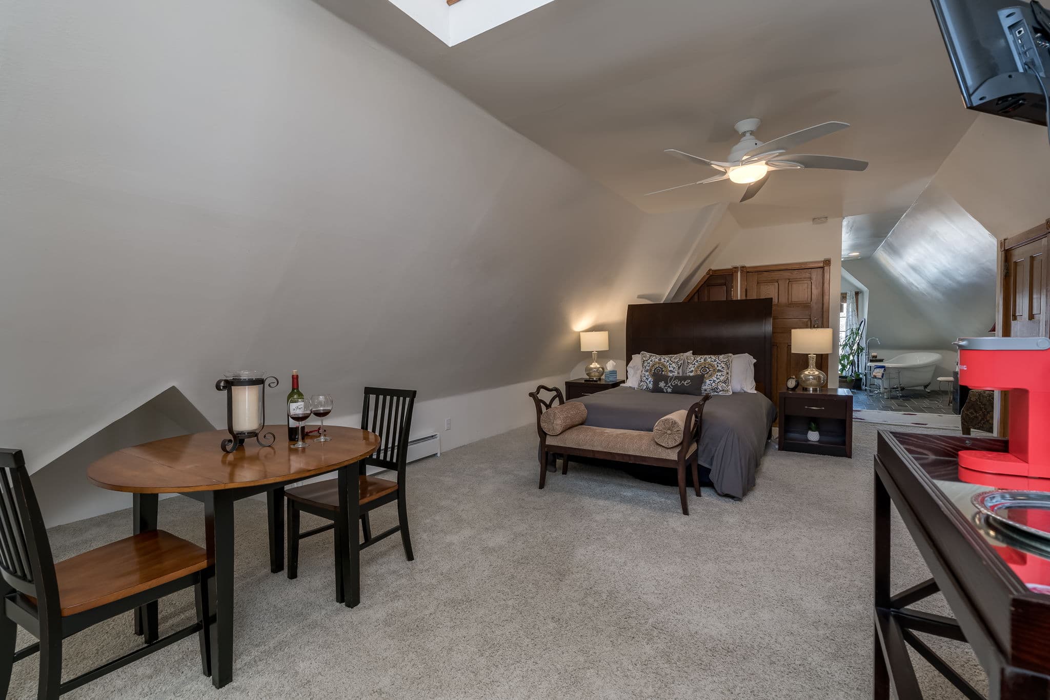 A cozy attic bedroom featuring a bed, dining table, and a ceiling fan.