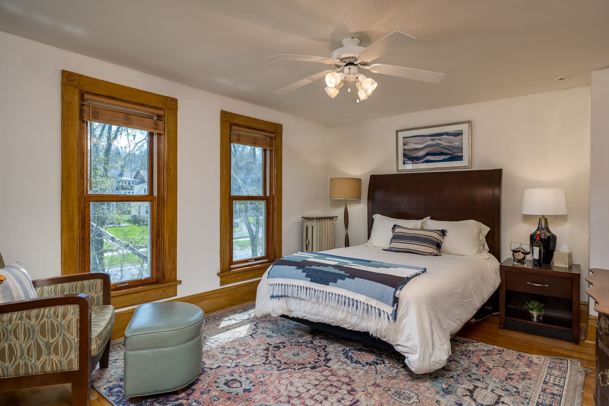 Cozy bedroom featuring a bed with a patterned blanket, two windows, a ceiling fan, and wooden accents.
