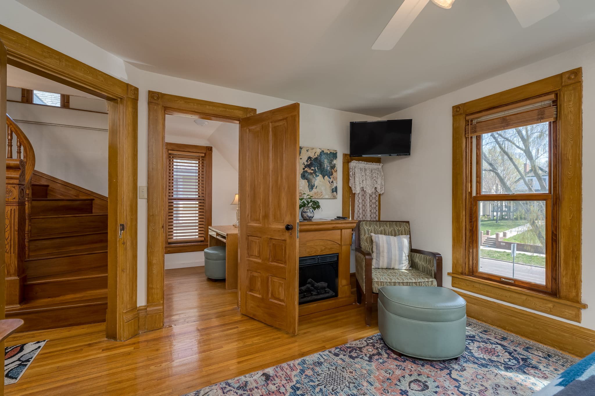 A cozy room featuring a seating area, a small fireplace, and a view through windows with wooden trim.