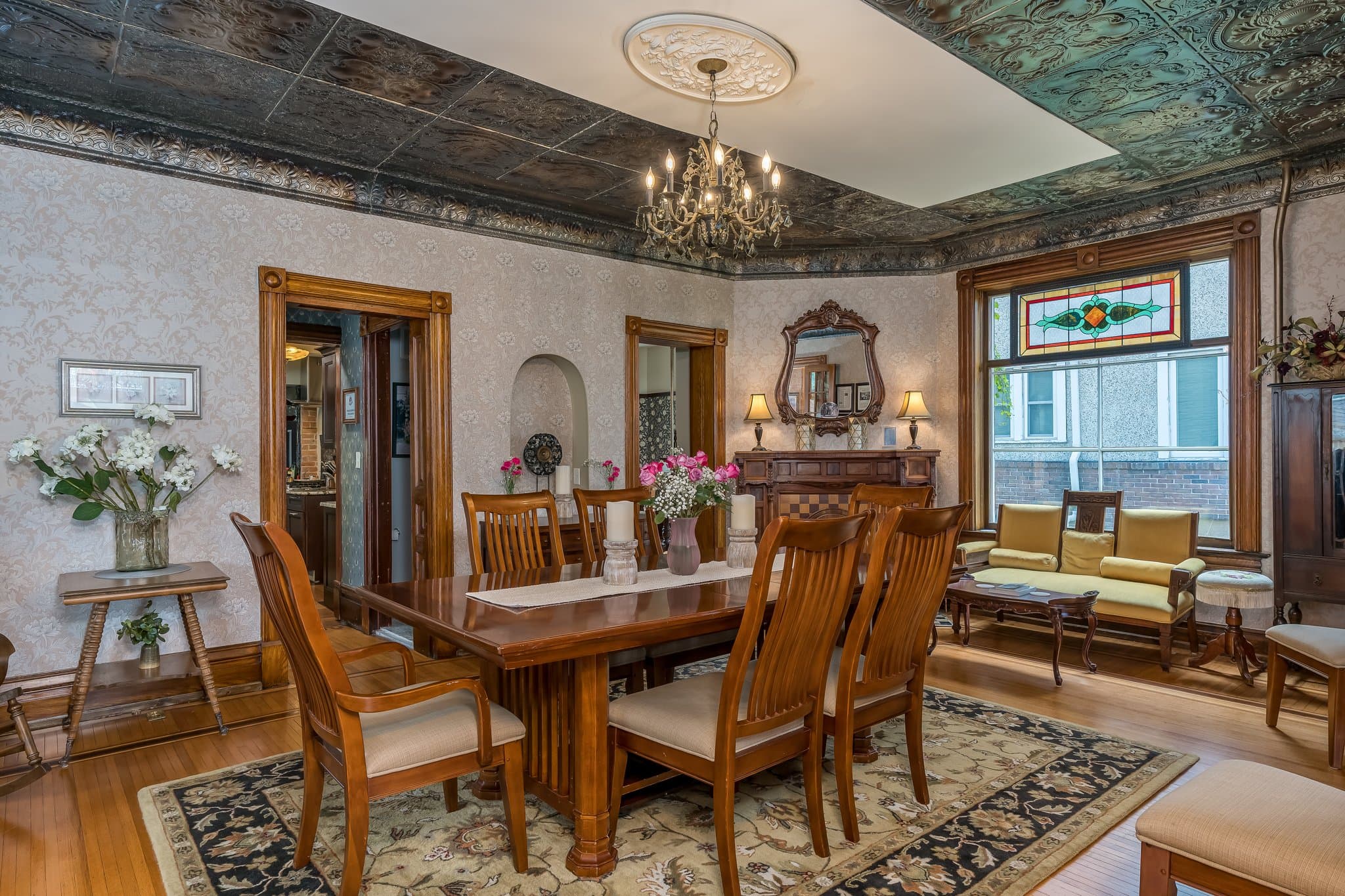 A spacious dining room featuring a wooden table, elegant chairs, floral decorations, and a vintage chandelier.
