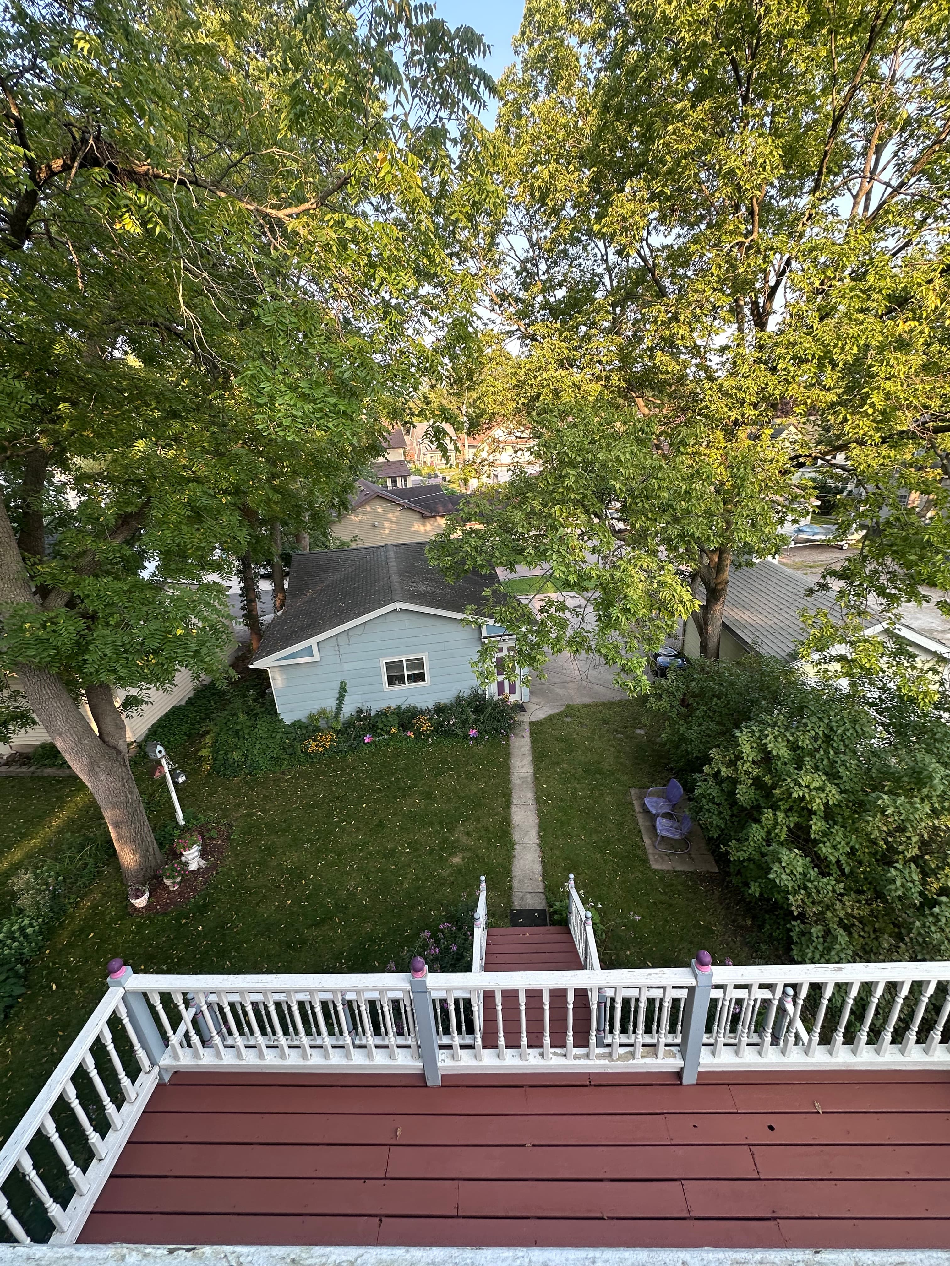 Aerial view of a backyard with green grass, trees, and a light blue house.