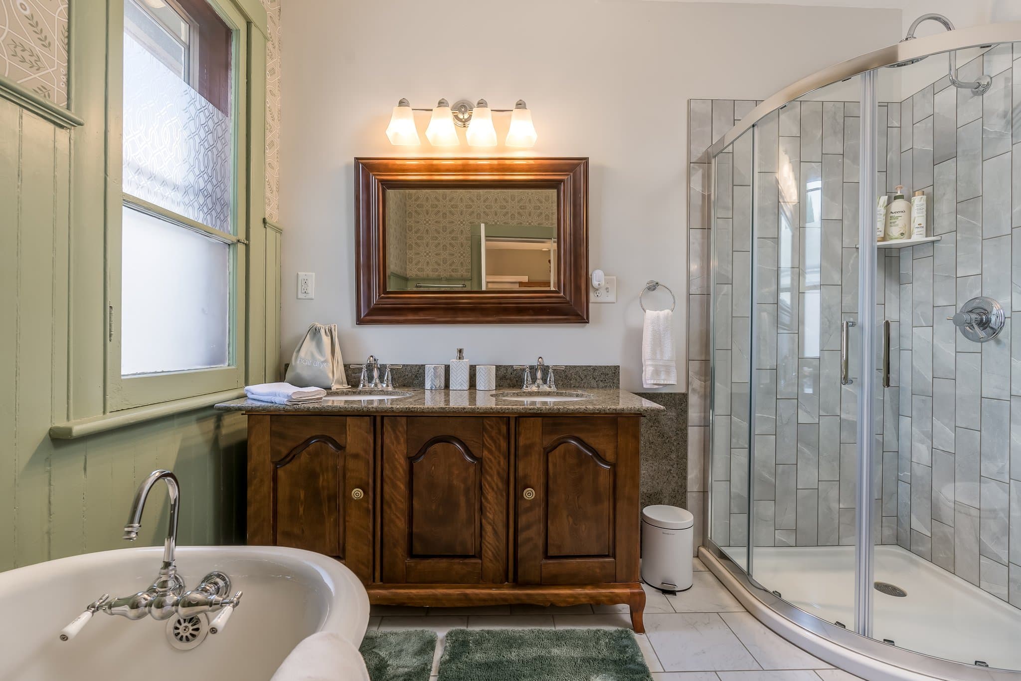 Bright bathroom featuring a vintage wooden vanity, a glass shower, and a freestanding bathtub.